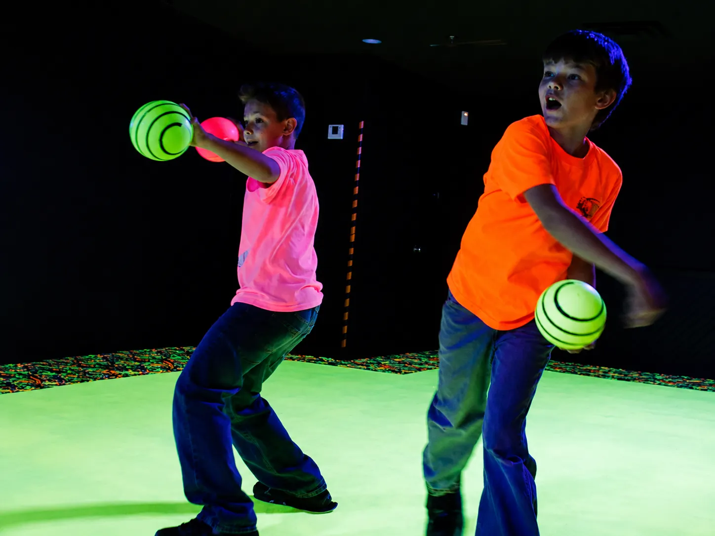 Things to do at Fun Slides. Two kids playing glow dodgeball with neon balls in a dark blacklight game room.