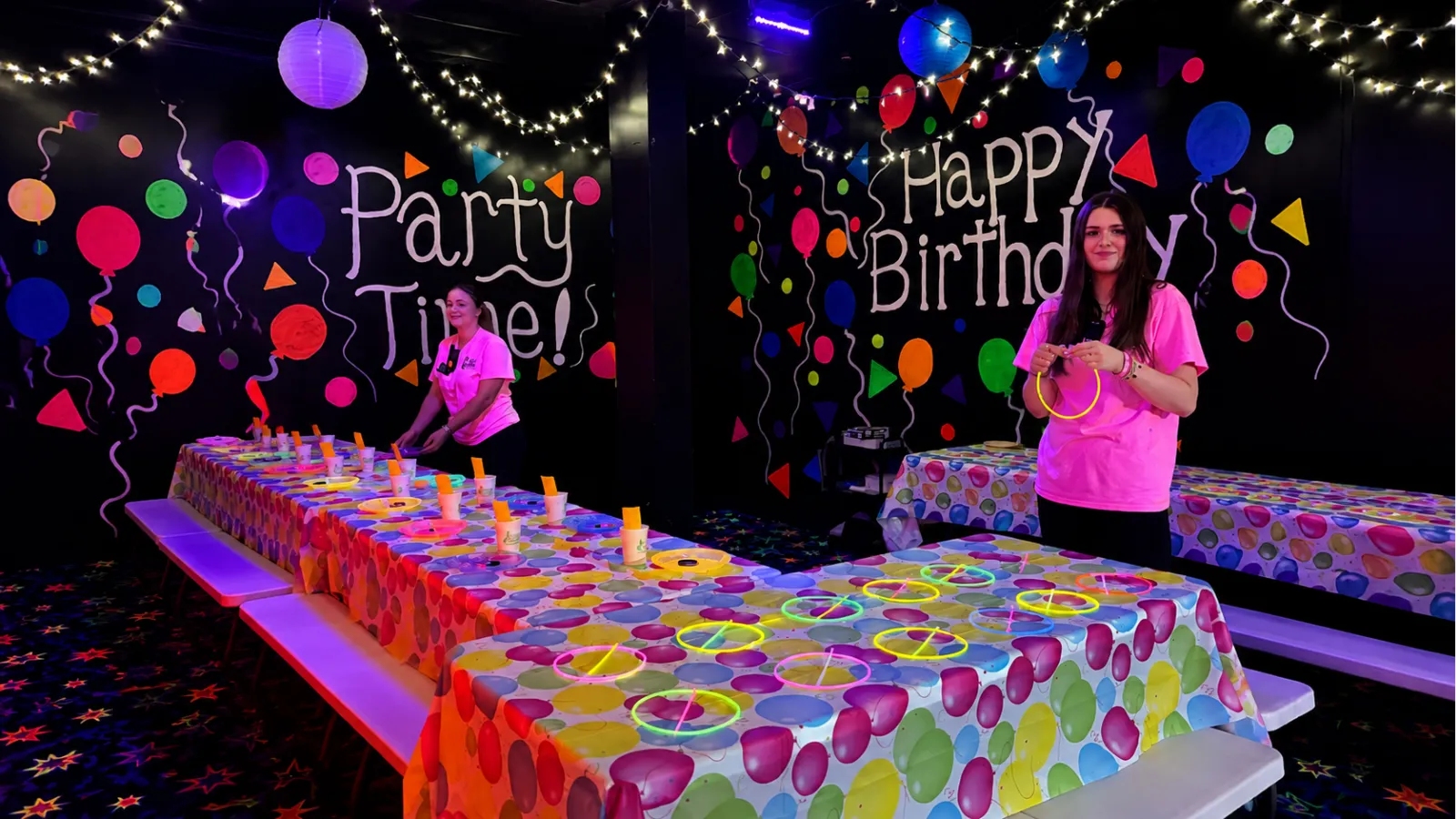 Fun Slides staff members setting up glow rings and party supplies on decorated tables in the blacklight birthday room.